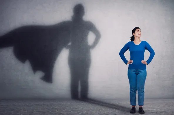 Frau mit selbstbewusster Haltung wirft einen Schatten in Form eines Superhelden – Symbol für die Verantwortung und Stärke des Wahlvorstands.