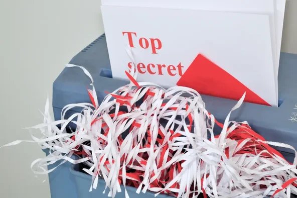 Dokument mit Aufschrift ‚Top Secret‘ in einem Aktenvernichter – Symbol für die Vernichtung verspäteter Briefwahlumschläge bei der Betriebsratswahl.