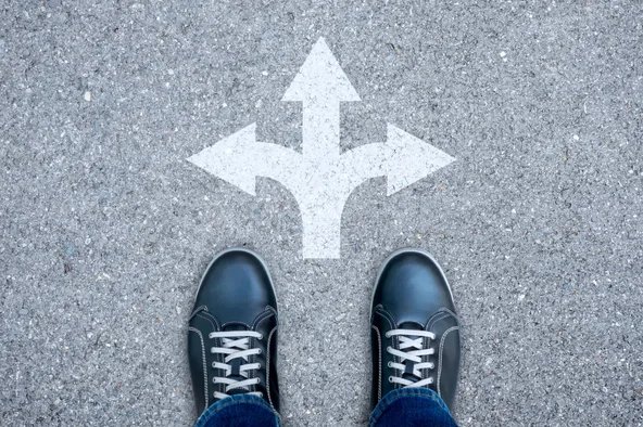 Schuhe stehen vor einer Weggabelung mit drei Pfeilen – Symbol für die Wahl des richtigen Wahlverfahrens bei der Betriebsratswahl.