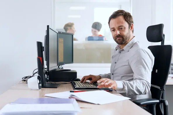 Mann arbeitet am Computer mit Dokumenten auf dem Schreibtisch – Symbol für die Berechnung der Betriebsratsgröße.