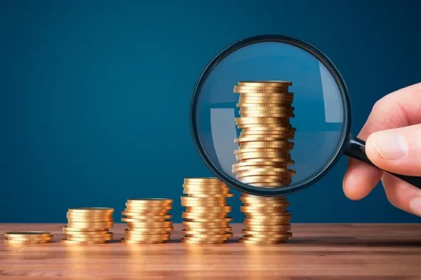 Gestapelte Münzen mit Lupe – Symbol für die Analyse und Transparenz der Kosten einer Betriebsratswahl.
